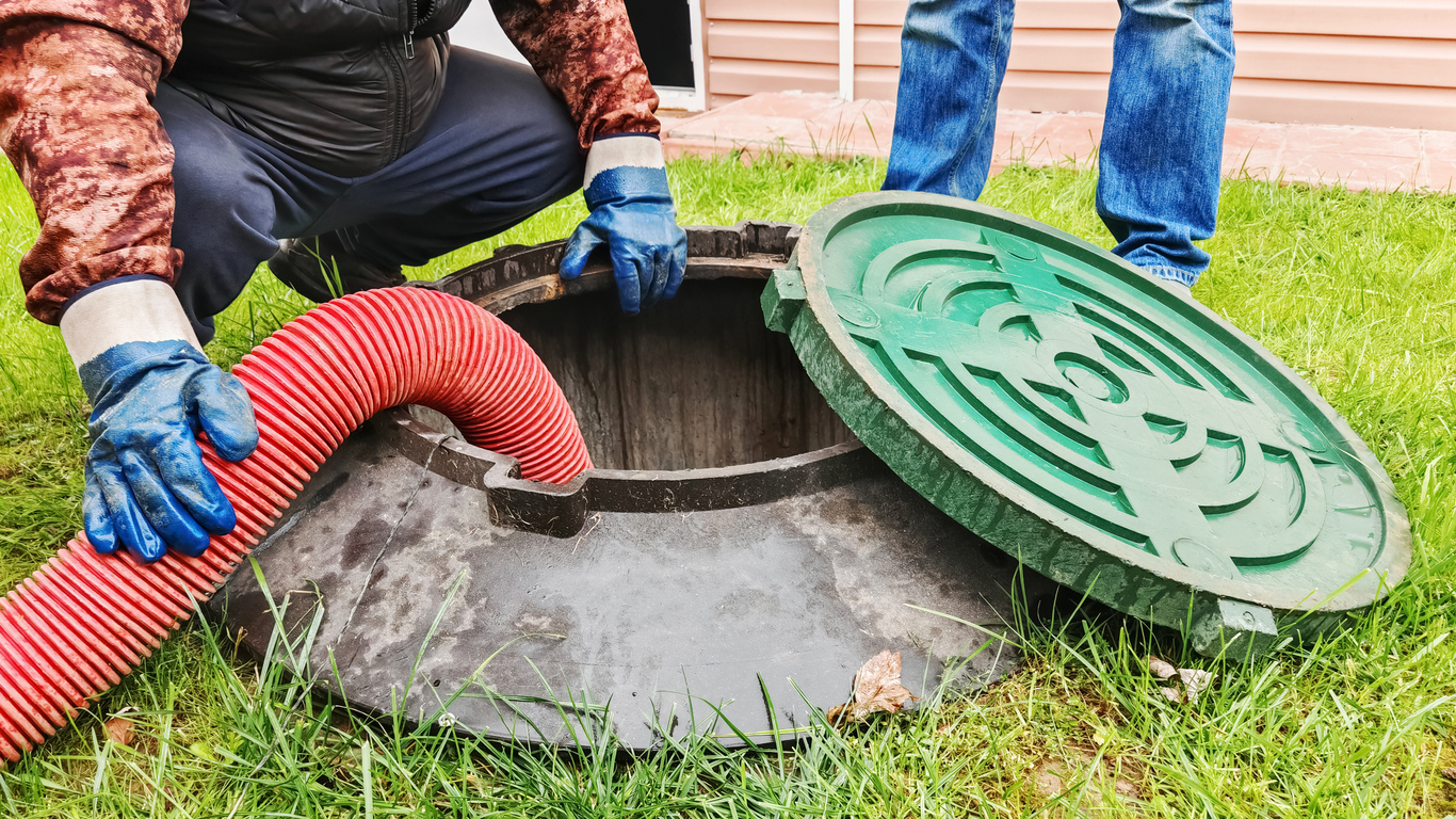 Maintenance of rural sewerage systems, pumping out wastewater using a submersible sewage pump.Pipe in a drain hole, servicing a septic tank in a backyard, removing waste with a hose and ensuring proper maintenance.