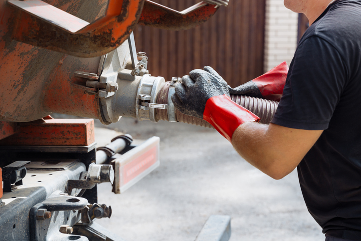 A technician in gloves connects equipment to a septic truck for service work at a home site. Septic tank service. Sewage Tank truck.